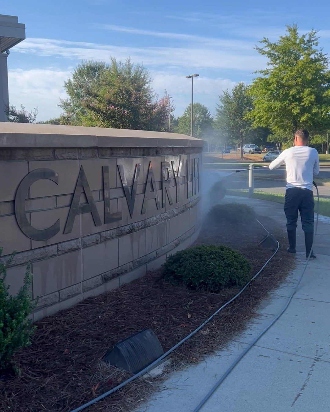 Stan pressure washing the stone Calvary sign, spray rising off the lettering